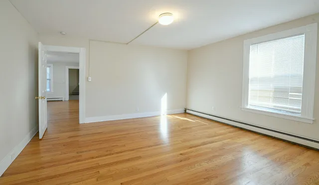 a view of an empty room with wooden floor and a window