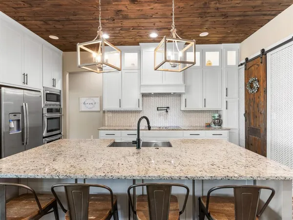 a kitchen with stainless steel appliances granite countertop a sink a stove a refrigerator cabinets and chairs