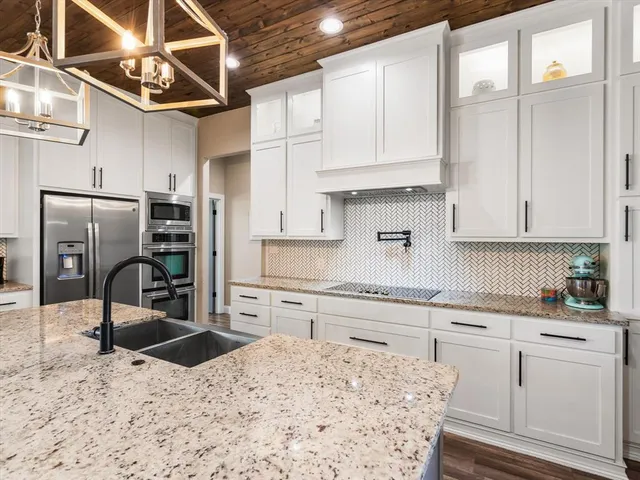 a kitchen with stainless steel appliances kitchen island granite countertop a refrigerator a sink dishwasher and white cabinets with wooden floor