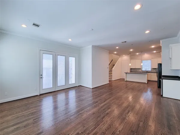 a view of an empty room with wooden floor and a kitchen