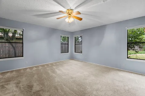 a view of an empty room with window and chandelier fan