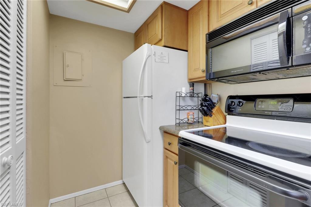 600 Neapolitan Way, Unit 345 Naples, FL 34103 - Photo 19 of 43 Kitchen with black microwave, range with electric stovetop, light tile patterned floors, freestanding refrigerator, and baseboards