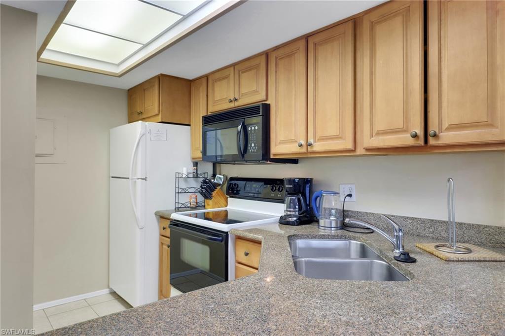 600 Neapolitan Way, Unit 345 Naples, FL 34103 - Photo 20 of 43 Kitchen with range with electric cooktop, black microwave, a sink, light tile patterned floors, and freestanding refrigerator