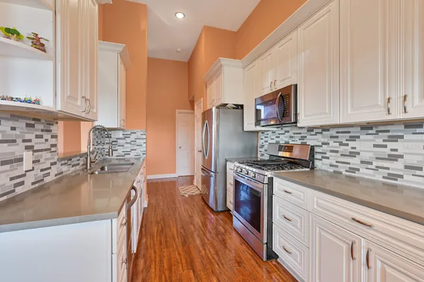 a kitchen with stainless steel appliances granite countertop a stove top oven a sink dishwasher and a refrigerator with wooden floor