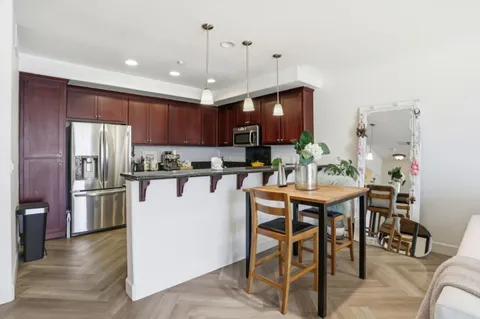 a kitchen with stainless steel appliances granite countertop a stove a refrigerator a kitchen island a dining table and chairs with wooden floor