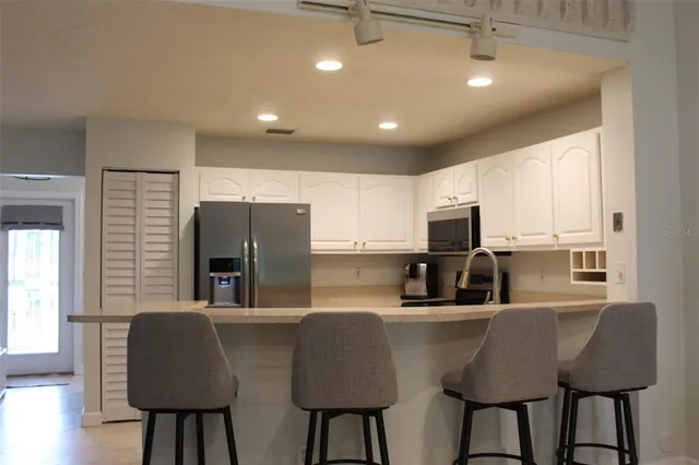 a kitchen with stainless steel appliances granite countertop a dining table chairs refrigerator and sink