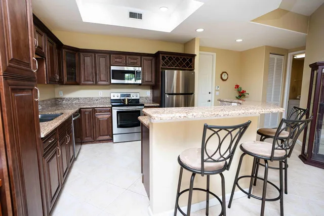 a kitchen with stainless steel appliances granite countertop a stove top oven a sink a refrigerator and chairs