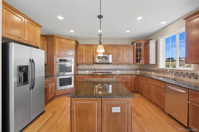 a kitchen with stainless steel appliances granite countertop a sink a stove a refrigerator cabinets and a large window