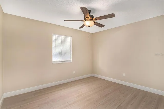 an empty room with wooden floor fan and windows