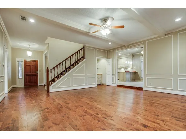a view of an empty room with wooden floor and a kitchen