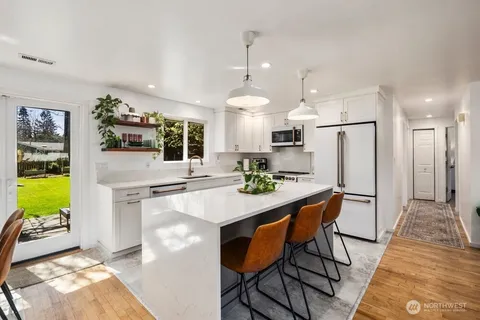 a kitchen with kitchen island a stove a refrigerator a oven a sink a dining table and chairs with wooden floor