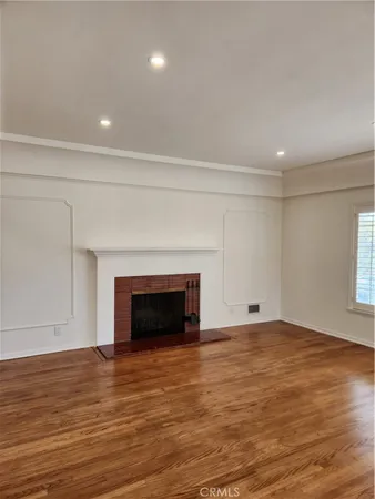 a view of an empty room with wooden floor fireplace and a window