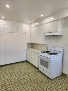 a kitchen with granite countertop a stove a sink and white cabinets