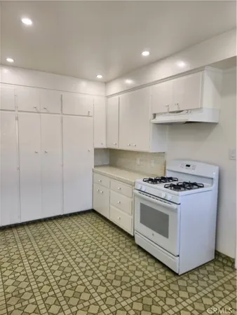a kitchen with granite countertop a stove a sink and white cabinets