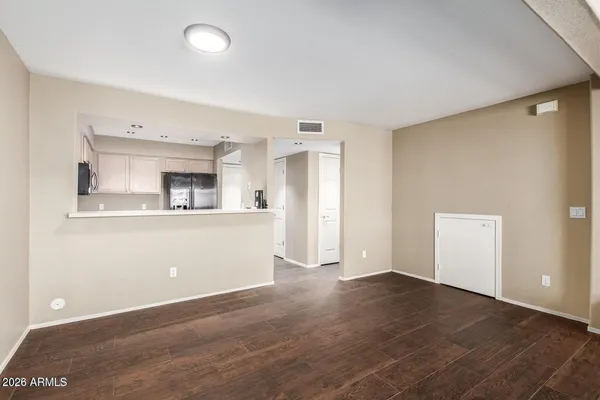 an empty room with wooden floor and kitchen view
