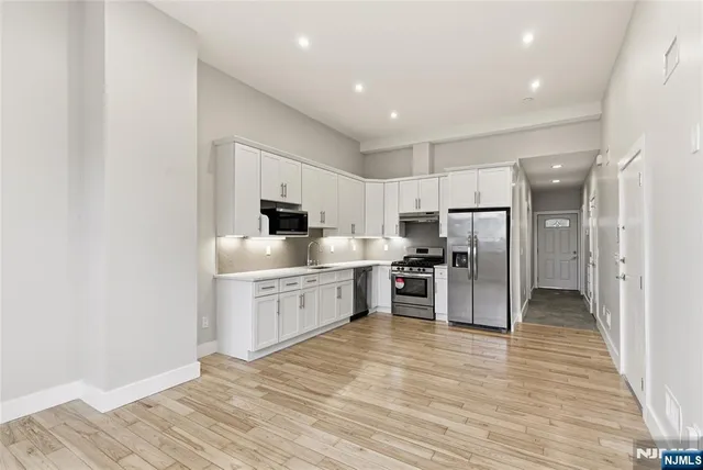 a room with stainless steel appliances kitchen island granite countertop a refrigerator and a sink