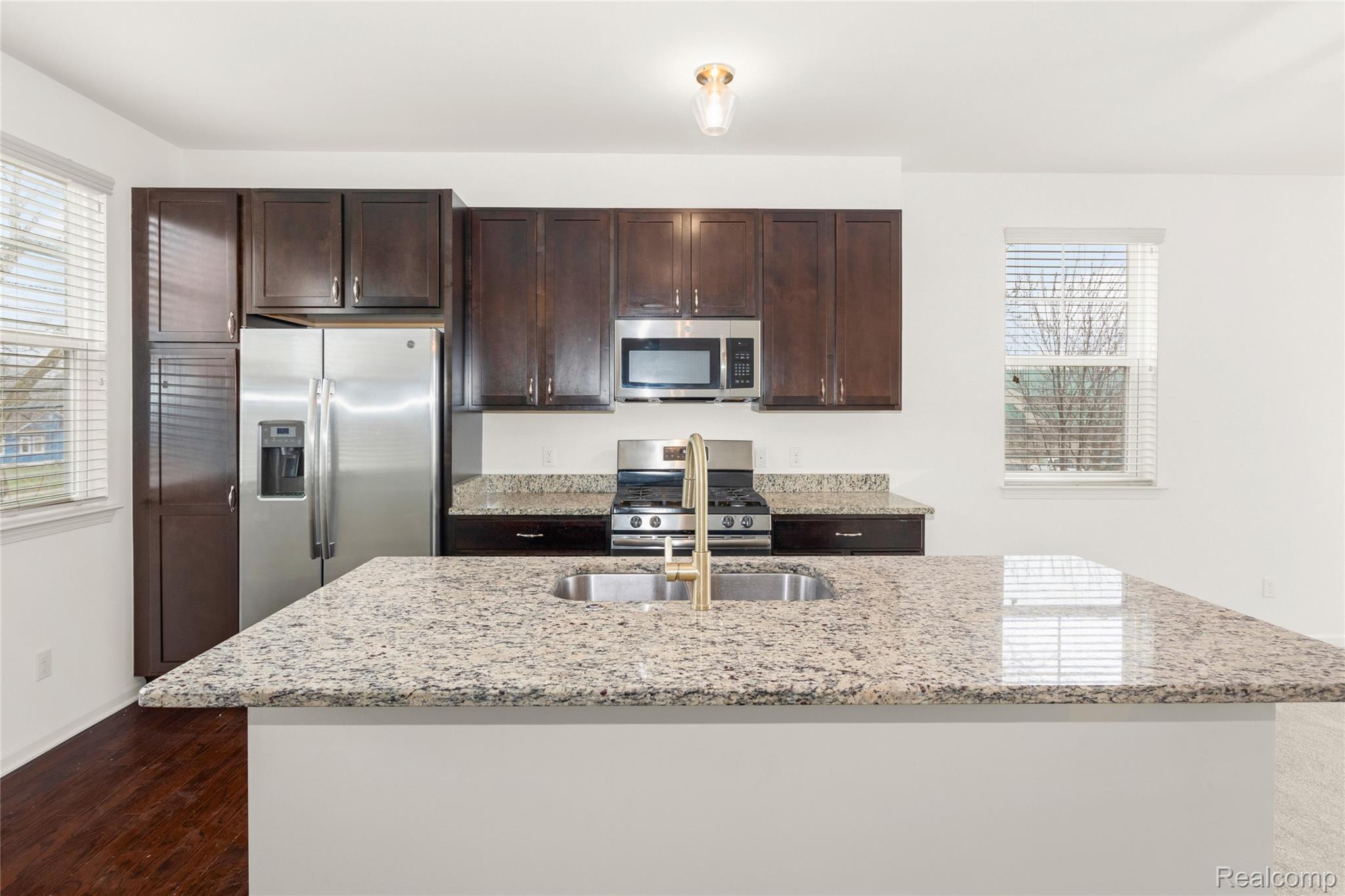 478 North Wixom Road Wixom, MI 48393 - Photo 8 of 26 Kitchen with dark wood finish cabinets, stainless steel appliances, light stone countertops, and a kitchen island with sink