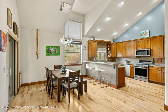 a kitchen with stainless steel appliances kitchen island granite countertop a refrigerator a stove a sink a dining table and chairs with wooden floor