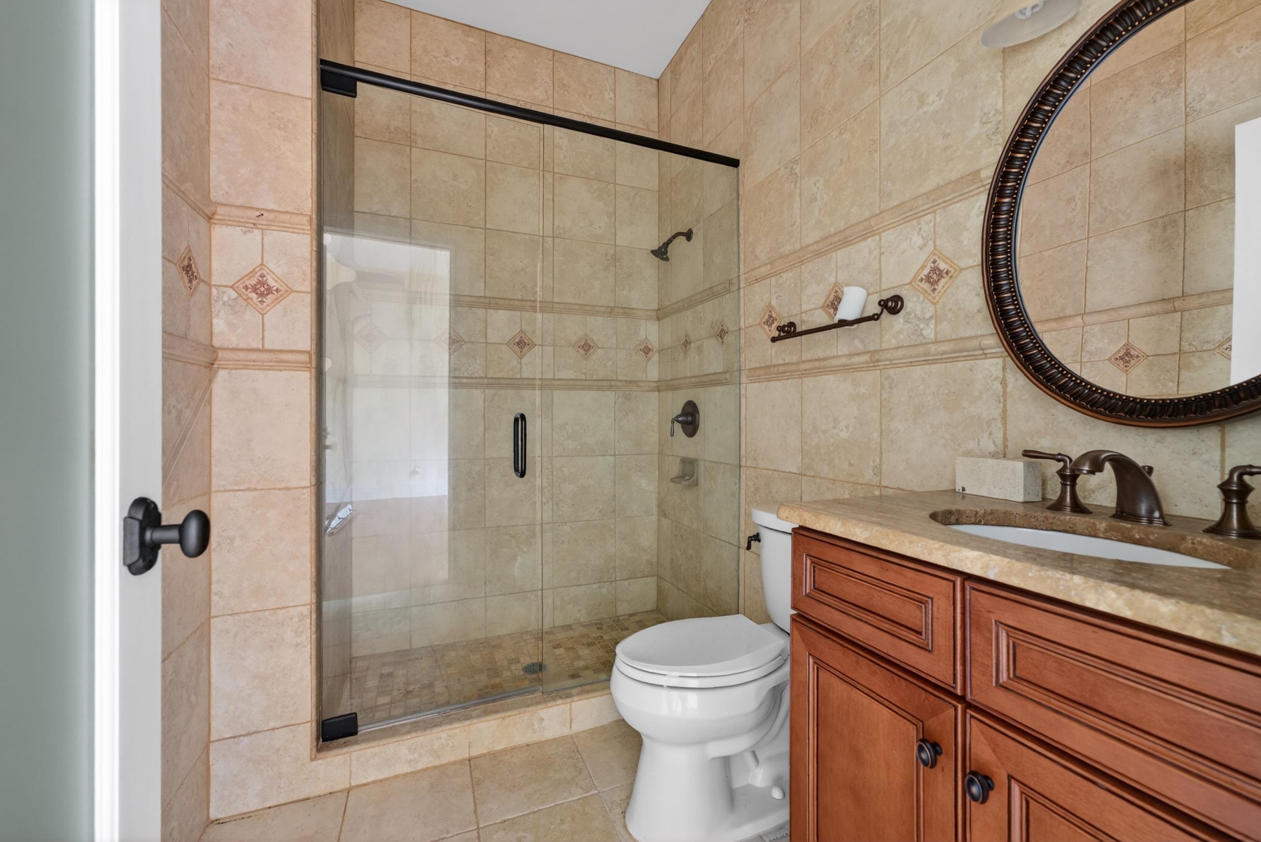 530 West Raines Road Memphis, TN 38109 - Photo 31 of 38 Tiled bathroom featuring a glass-enclosed shower, a vanity with a built-in sink, a circular mirror, and bronze fixtures