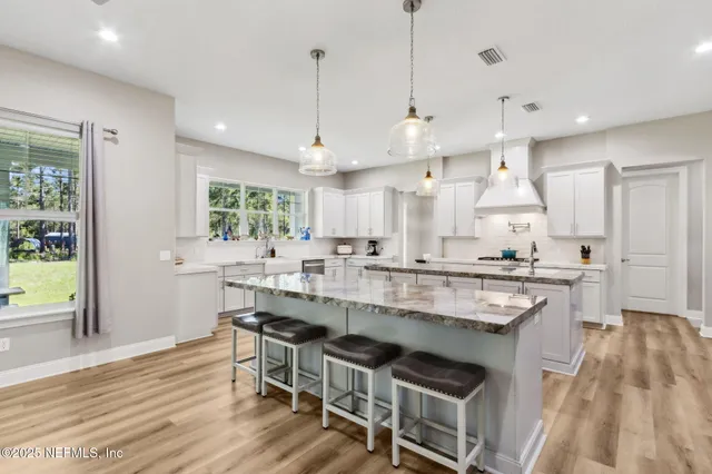 a kitchen with stainless steel appliances granite countertop a refrigerator a sink dishwasher a stove and white cabinets with wooden floor