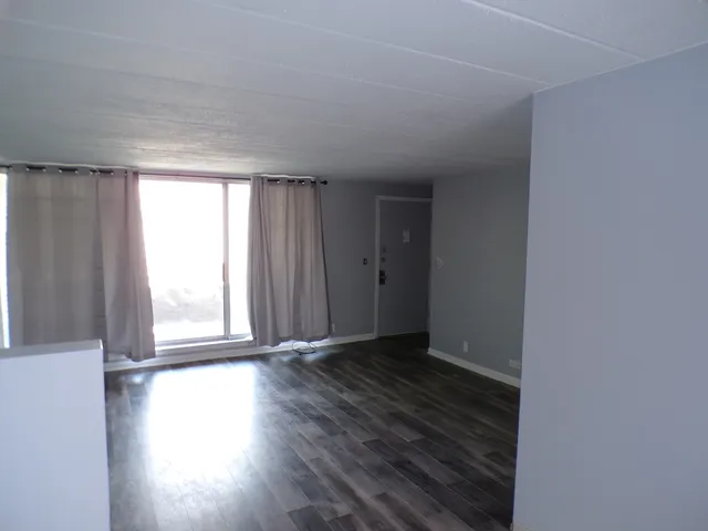 an empty room with wooden floor and windows with curtains