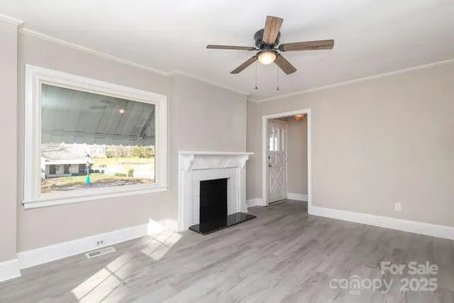 a view of an empty room with wooden floor fireplace and a window