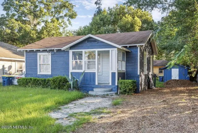 a view of a brick house with a big yard plants and large tree