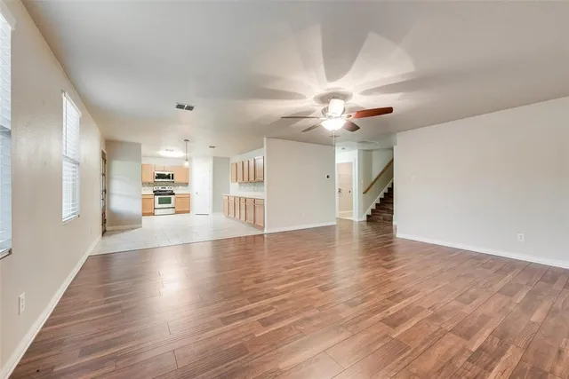 a view of a livingroom with wooden floor a ceiling fan and windows