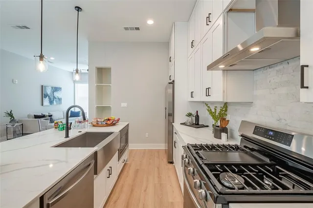 a kitchen with stainless steel appliances granite countertop a stove a sink dishwasher and white cabinets with wooden floor
