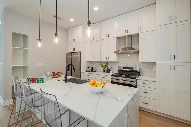 a kitchen with stainless steel appliances a stove a sink a center island a stove and white cabinets with wooden floor