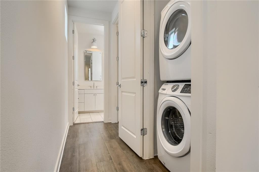 2624 Metcalfe Road, Unit 7 Austin, TX 78741 - Photo 27 of 31 Hallway featuring wood-finish flooring, a stacked washer and dryer unit, and a bathroom entry with white vanity and wall-mounted mirror