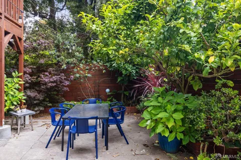 a backyard of a house with table and chairs potted plants and large tree