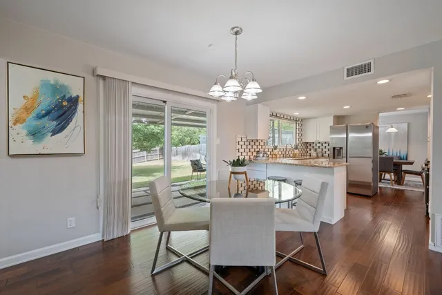 a dining room with wooden floor a chandelier a glass table and chairs