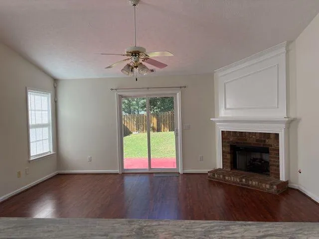 a view of an empty room with wooden floor fireplace and a window
