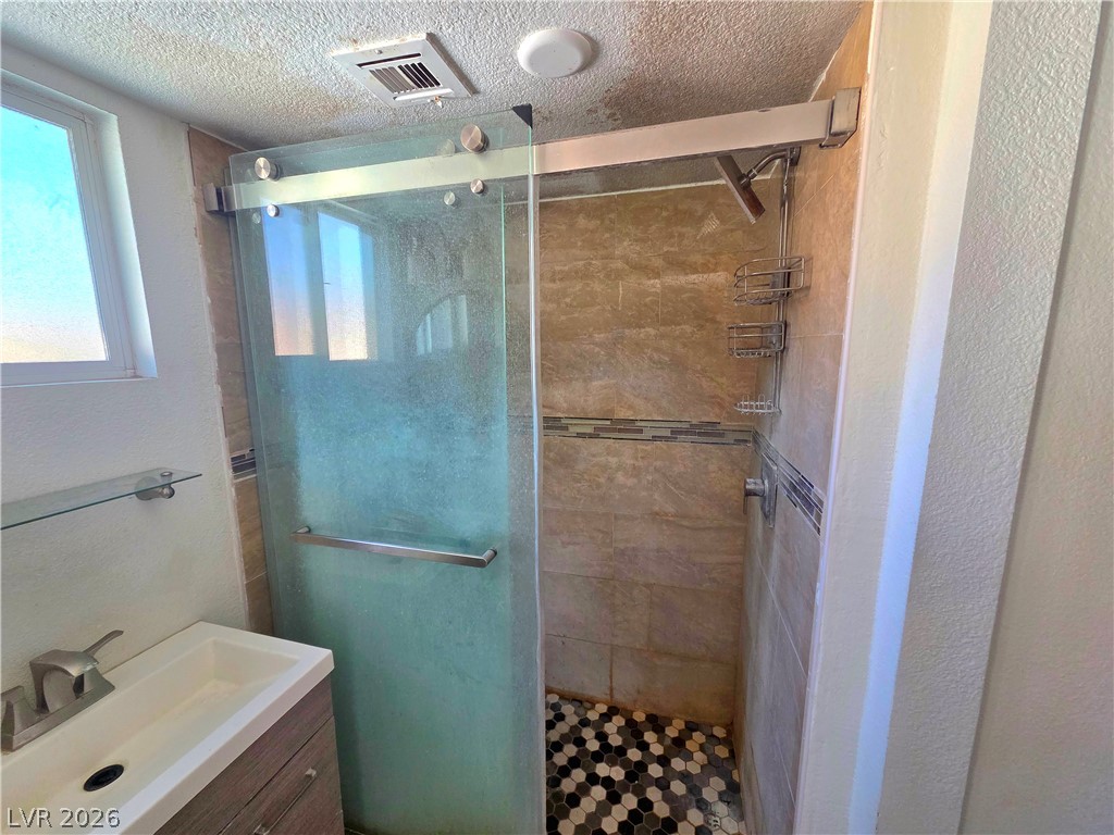 3648 Bronco Road Las Vegas, NV 89103 - Photo 13 of 24 A well-lit primary bathroom features a tiled walk-in shower with a glass enclosure and a contemporary vanity.