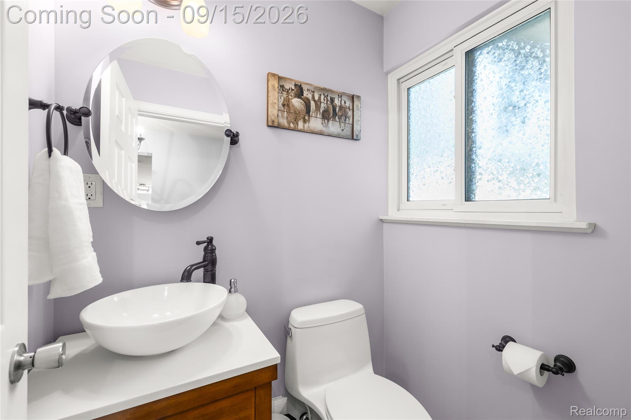 Modern vanity with a vessel sink, dark bronze fixtures, an oval mirror, and a frosted window