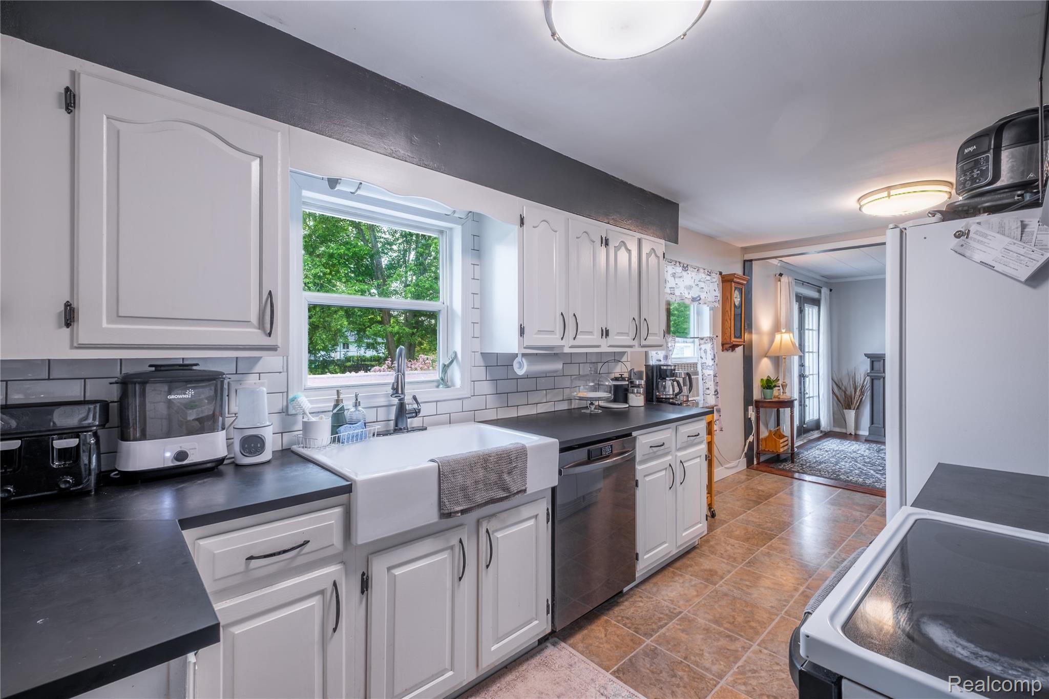 7800 Maple Street Birch Run, MI 48415 - Photo 8 of 29 Kitchen featuring white cabinetry, dark countertops, a white farmhouse sink, subway tile backsplash, and tile flooring