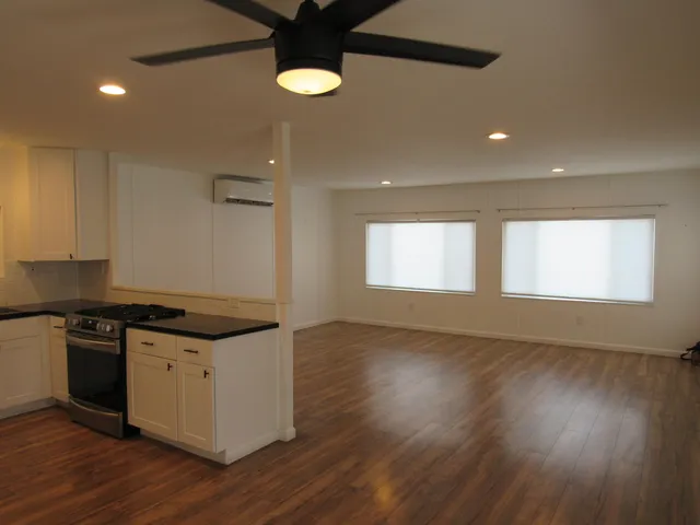 an empty room with wooden floor a ceiling fan and windows