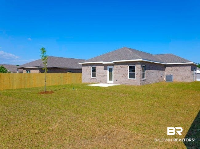 13791 Logan Place Foley, AL 36535 - Photo 5 of 25 Expansive backyard featuring a privacy fence, a newly planted tree, a concrete patio, and a brick exterior home with a shingled roof and white-framed windows