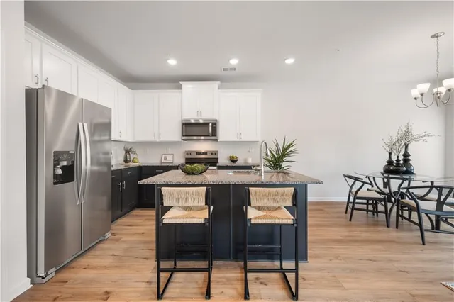 a kitchen with stainless steel appliances a dining table chairs refrigerator and cabinets