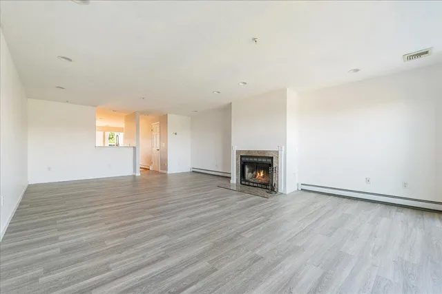 a view of an empty room with wooden floor fireplace and a window