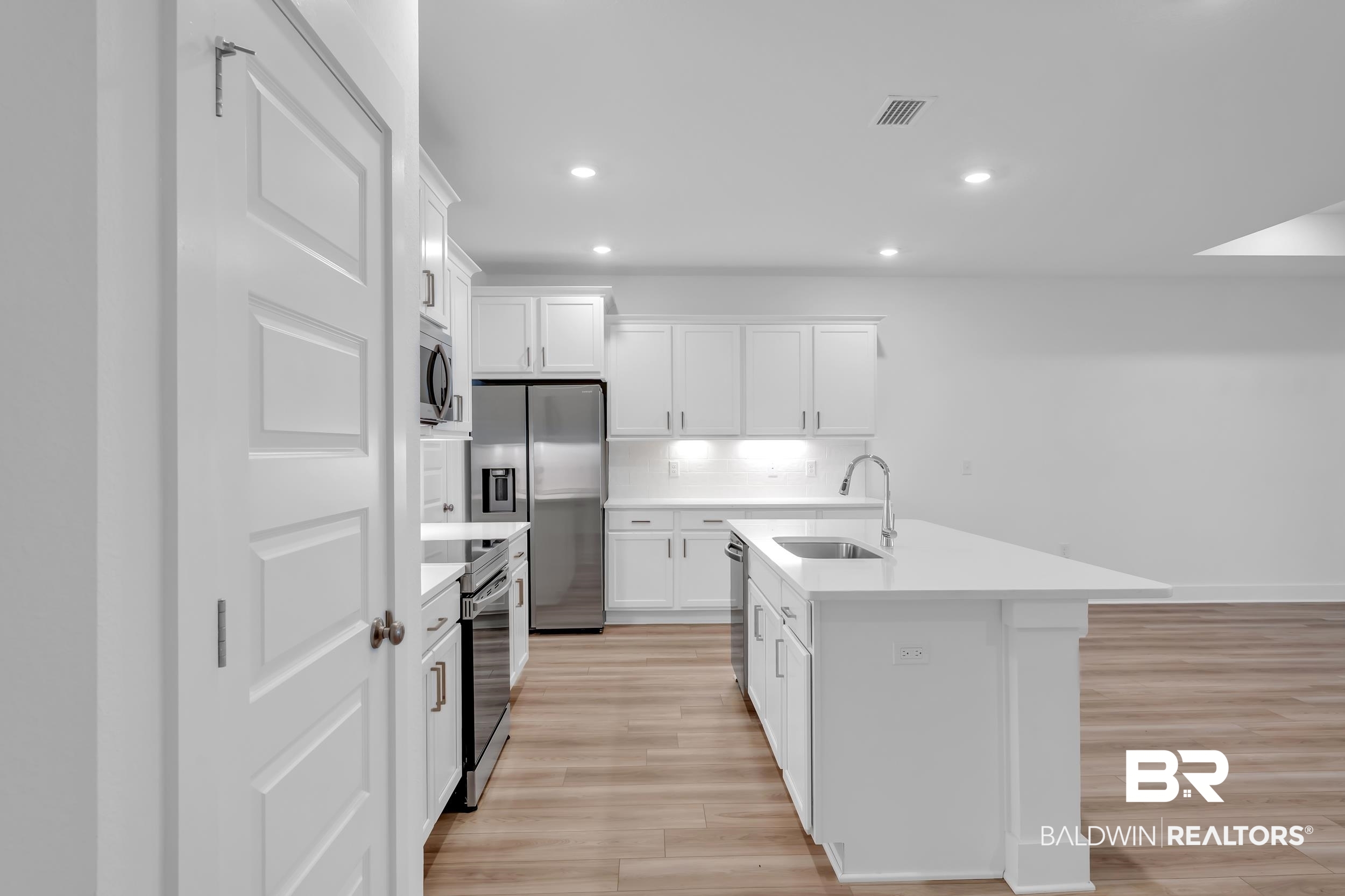 9933 Weller Cove Foley, AL 36535 - Photo 10 of 36 Modern kitchen featuring white cabinetry, stainless steel appliances, a center island with sink, quartz countertops, and wood-finish flooring
