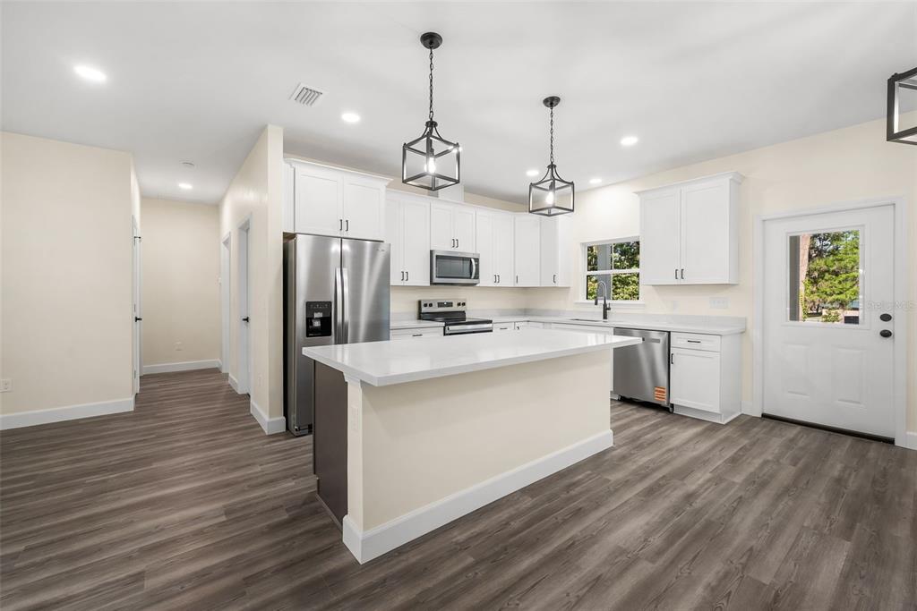 332 Southeast 3rd Avenue Melrose, FL 32666 - Photo 11 of 36 a kitchen with stainless steel appliances kitchen island a refrigerator a sink dishwasher a stove and white cabinets with wooden floor