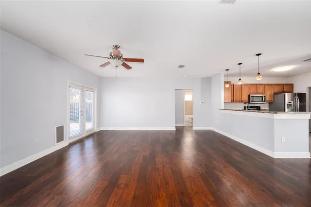 a view of an empty room with wooden floor and a kitchen