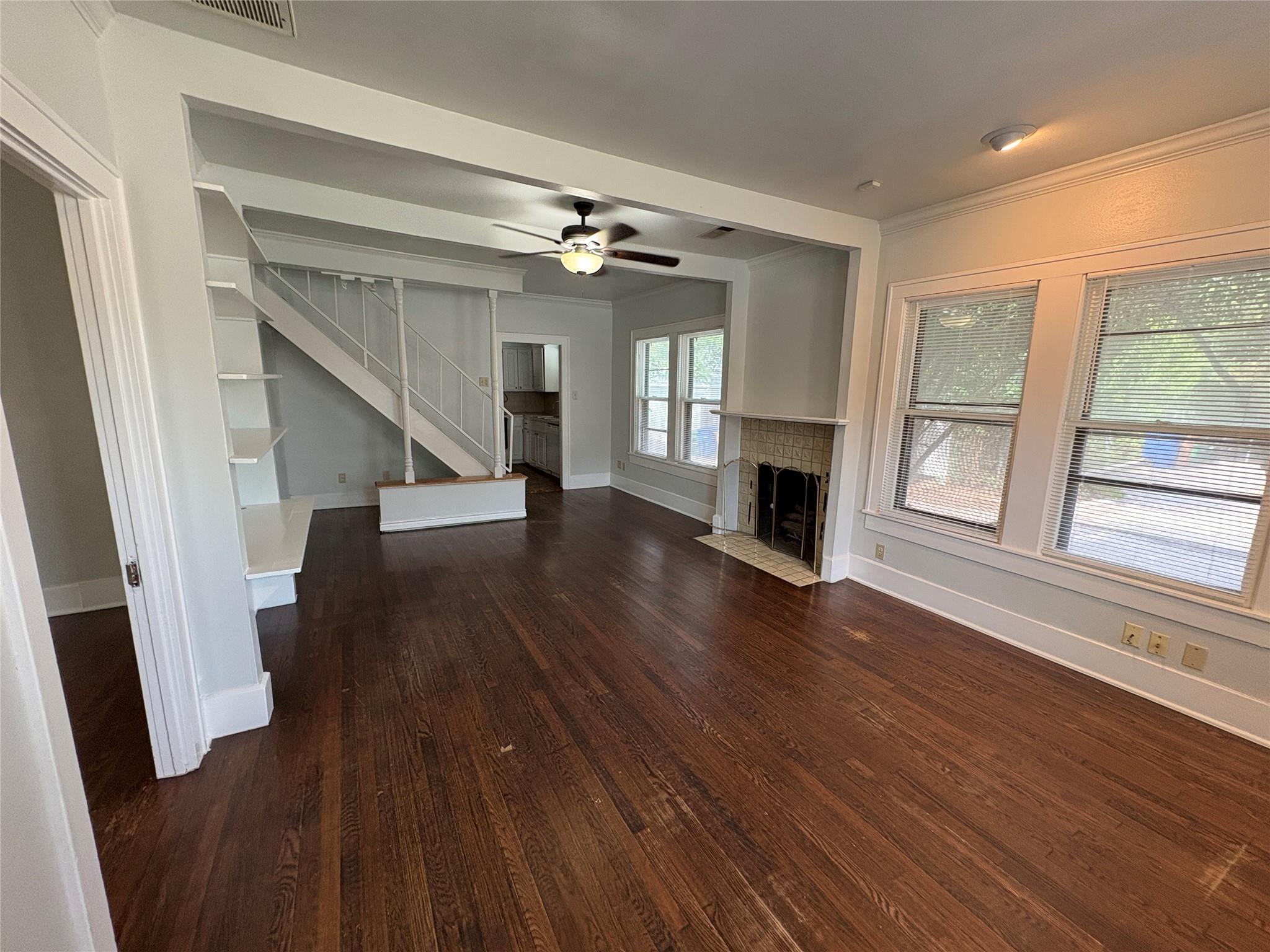 915 West 29th Street Austin, TX 78705 - Photo 2 of 20 Hardwood flooring extends throughout this expansive room, featuring a tile-surround fireplace with a hearth, multiple windows, and a ceiling fan with integrated lighting