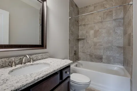 a bathroom with a granite countertop bathtub shower sink vanity and toilet
