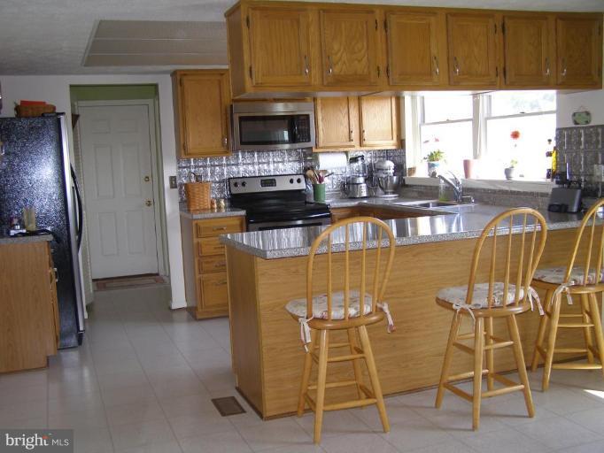 1203 Brookview Road Towson, MD 21286 - Photo 7 of 25 a kitchen with stainless steel appliances granite countertop a stove a refrigerator a sink a dining table and chairs with wooden floor