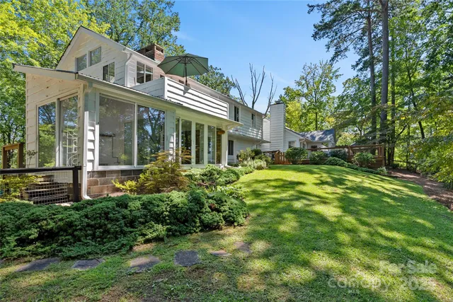 a view of a white house next to a yard with plants and trees