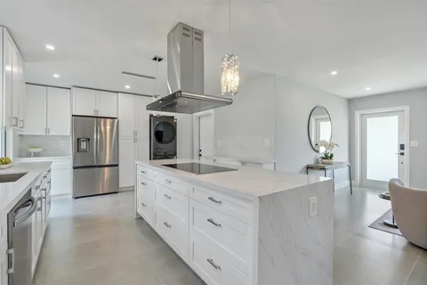 a kitchen with stainless steel appliances kitchen island granite countertop a refrigerator a sink dishwasher a dining table and chairs with wooden floor