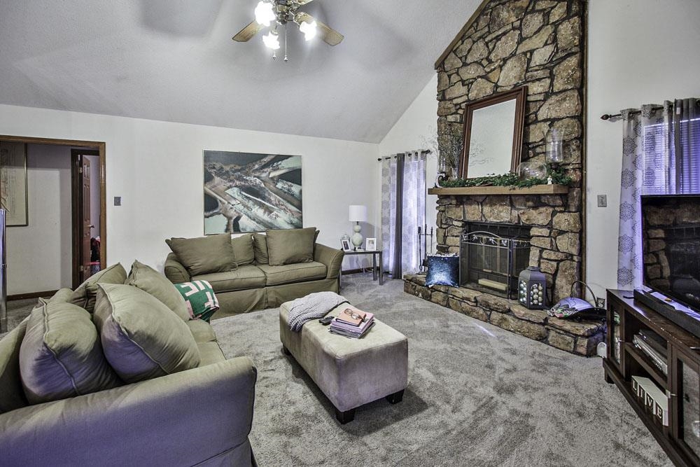 Living room with ceiling fan, high vaulted ceiling, carpet, and a fireplace